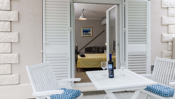 Ein Zimmer mit einem Bett, einem Tisch mit Flasche und Glas sowie einem Stuhl mit gepunktetem Kissen.