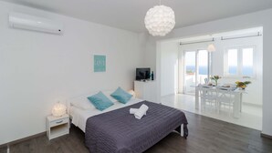 A modern bedroom with a bed, bedside table, and a view of the dining area. - Cin & Co Central Apartments (Dubrovnik)