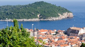 A coastal town with a prominent hill, red-roofed buildings, and a clear view of the sea. - Cin & Co Central Apartments (Dubrovnik)