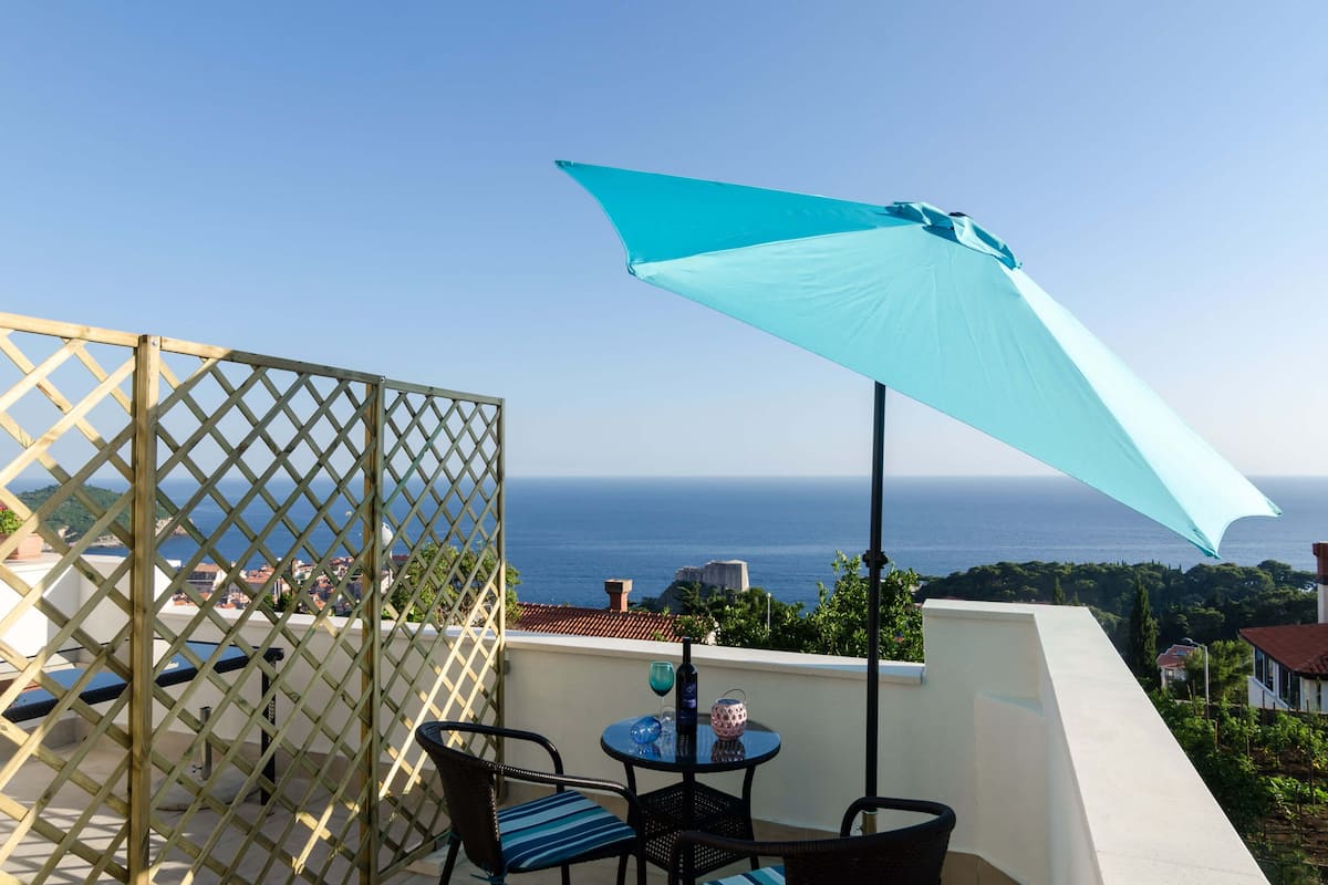 A balcony with a view of the sea, a table with chairs, and a large umbrella.