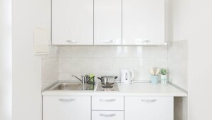 A kitchen with white cabinets, a sink, a stove, and a kettle. - Cin & Co Central Apartments (Dubrovnik)