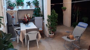 Un pequeño y acogedor patio con una mesa y sillas, rodeado de plantas en macetas y una planta colgante.