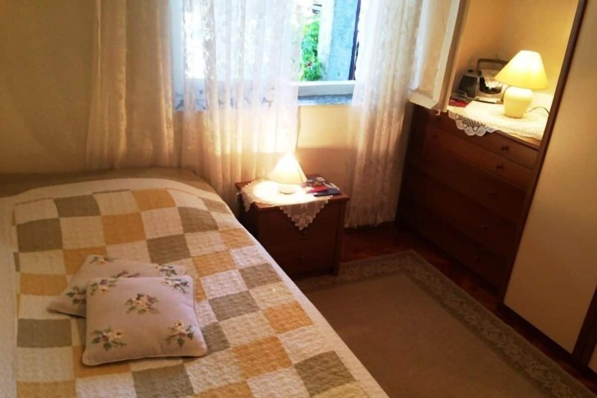 A bedroom with a checkered bedspread, a floral pillow, a bedside table with a lamp, and a dresser.