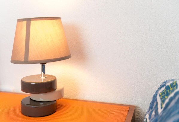 A table lamp with a cylindrical base and a conical shade on an orange surface.