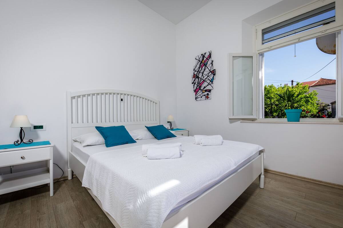 Quarto com cama, duas mesas de cabeceira, uma janela e vista para o verde lá fora.