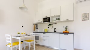 Cozinha moderna com armários brancos, micro-ondas e área de jantar com cadeiras brancas e almofadas amarelas.
