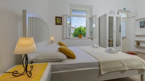 Quarto bem arrumado com uma cama, luminária de cabeceira, janela com vista para o verde e um guarda-roupa.