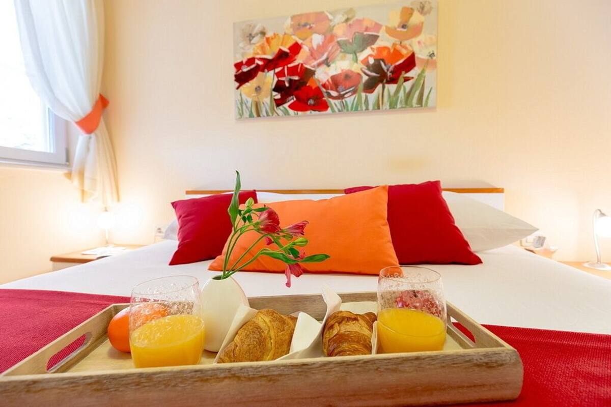A hotel room with a bed, a tray with breakfast items, and a painting on the wall.