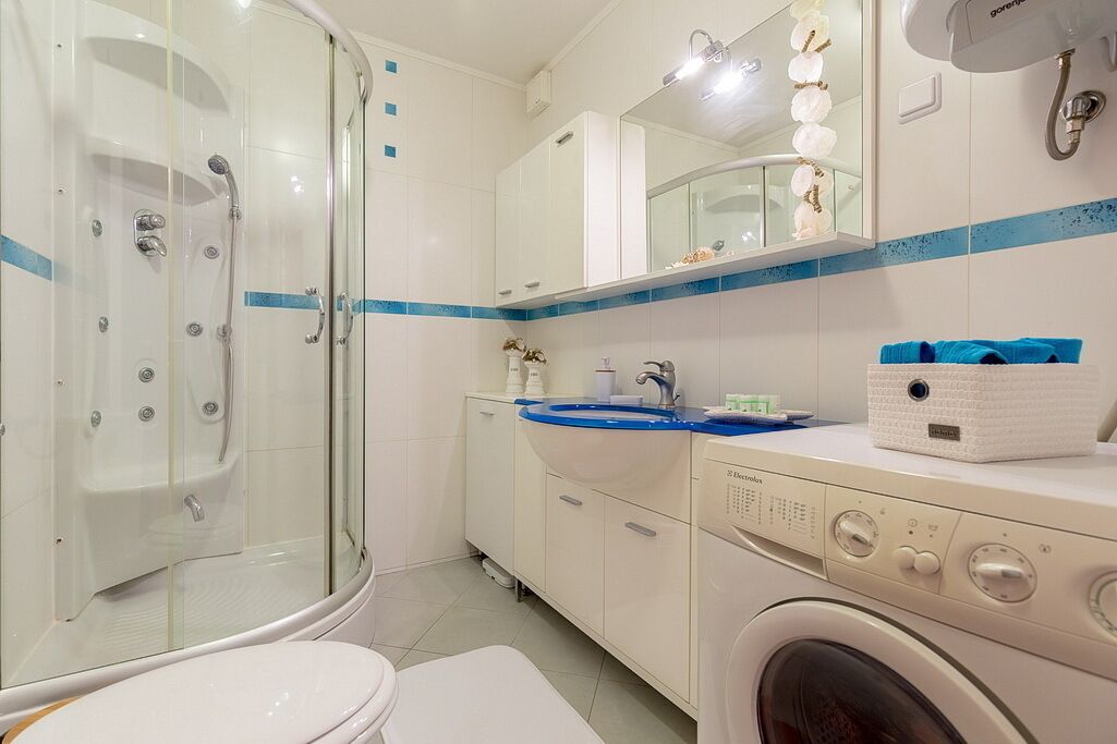 A modern bathroom with a glass-enclosed shower, a sink with a blue countertop, and a washing machine.