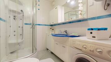A modern bathroom with a glass-enclosed shower, a sink with a blue countertop, and a washing machine.