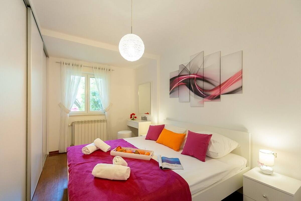 A hotel room with a bed, a bedside table with a lamp, a window with curtains, and a wall with abstract art.