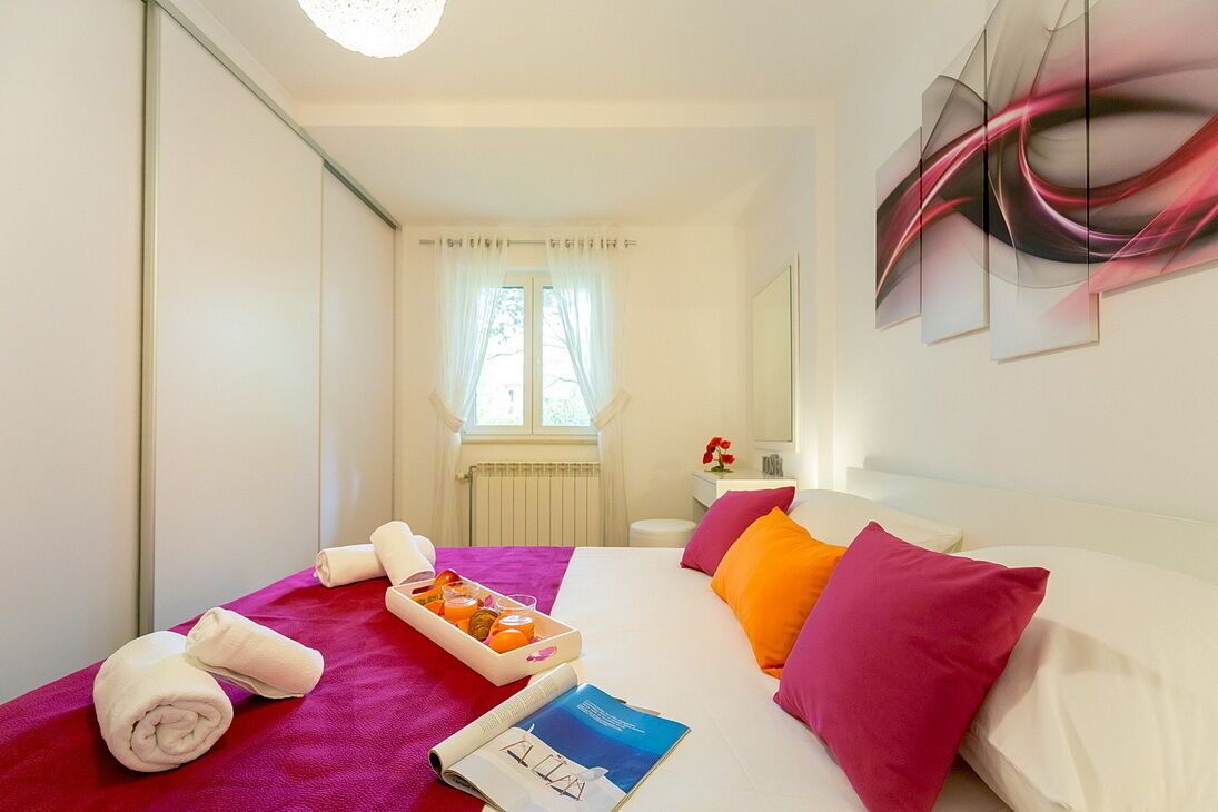 Ett hotellrum med en säng, ett sängbord, ett fönster med gardiner och en tavla på väggen.