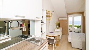 A compact kitchen with modern appliances, a dining area with a table and chairs, and a bed with a view of the sea. - Maraština Suites (Dubrovnik)