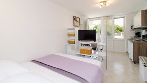 A modern hotel room with a bed, a television, a kitchenette, and a view of the outdoors. - Maraština Suites (Dubrovnik)