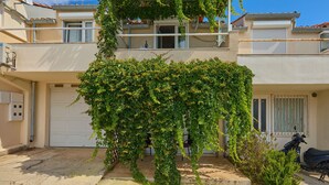 A two-story building with a garage door, a balcony with plants, and a parked scooter. - Maraština Suites (Dubrovnik)