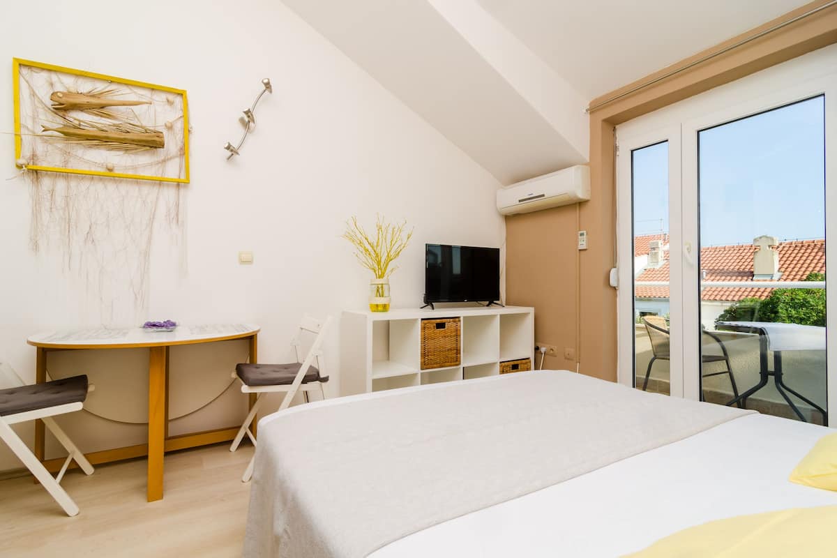 A hotel room with a bed, a desk with a chair, a television, and a balcony with a table and chairs.