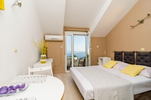Una habitación de hotel moderna con una cama, una mesita con un florero, una silla y vista al mar por una puerta corredera.