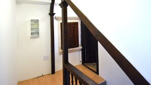 A wooden staircase with a dark finish, white walls, and a small shelf with items on the left side. - Studio Inn (Dubrovnik)