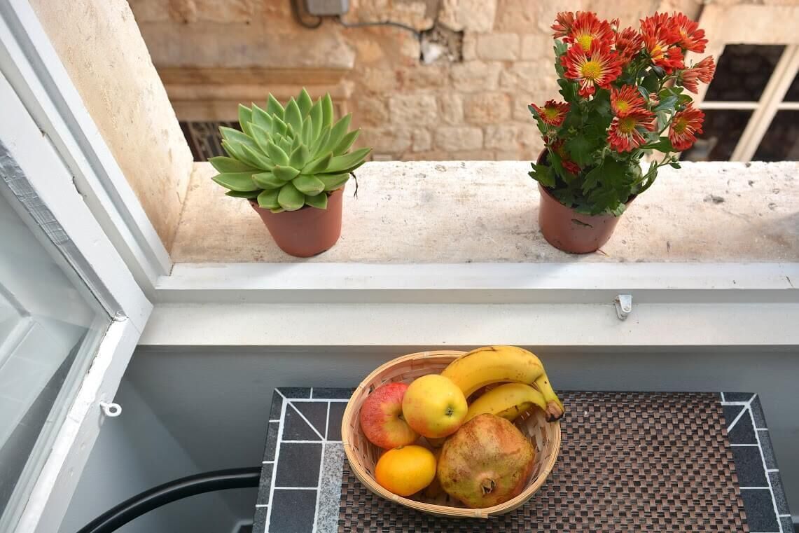 A window ledge with two potted plants and a fruit basket.