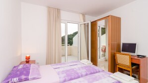 A hotel room with a bed, a desk with a computer, a mirror, and a view of the outdoors. - Apartments Feral (Mljet)