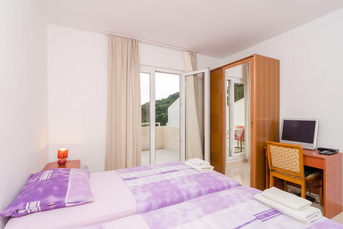 A hotel room with a bed, a desk with a computer, a mirror, and a view of the outdoors.