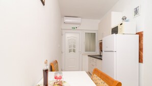 A compact kitchen with white cabinets, a white refrigerator, and a dining table with chairs. - Apartments Feral (Mljet)