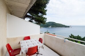 A balcony with a table and chairs, overlooking a coastal view with a tree and a distant island.