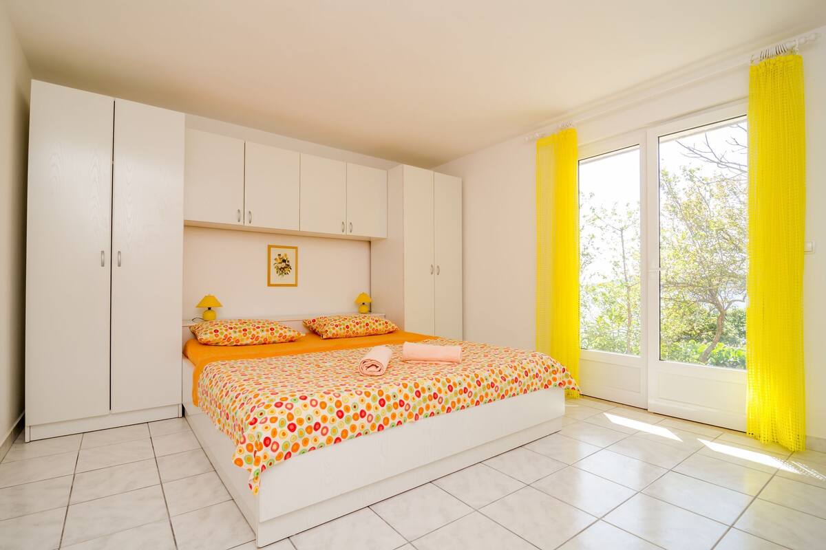 A bedroom with a bed, white wardrobe, and a window with yellow curtains.