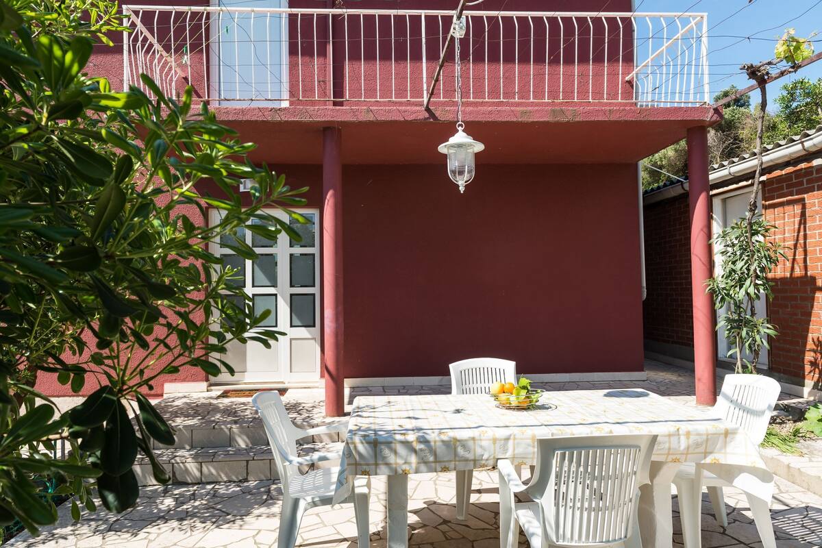 A patio with a table and chairs, a hanging lantern, and a red building with a balcony.