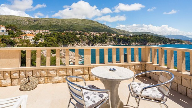 Un balcon avec une table ronde et deux chaises, donnant sur une ville côtière et la mer.