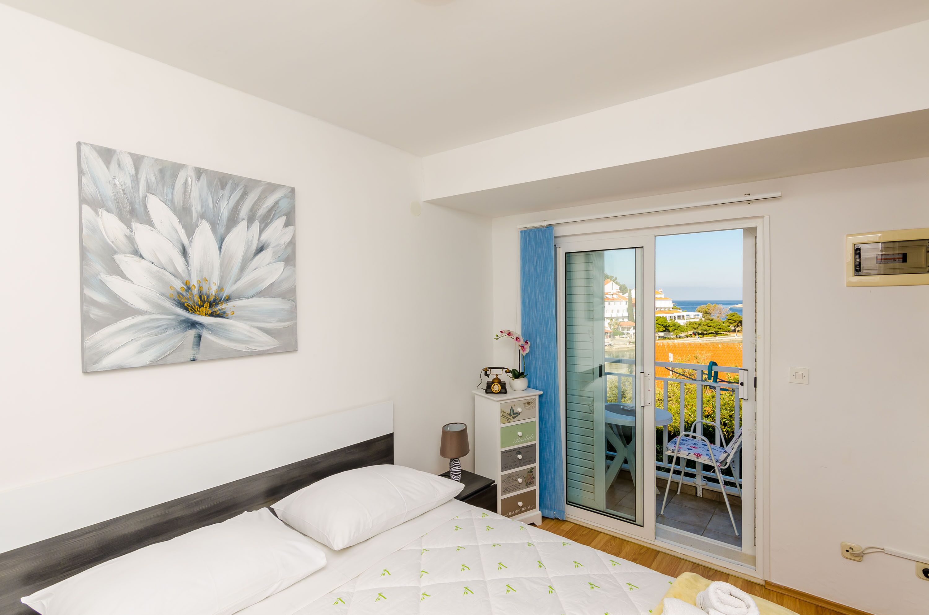A bedroom with a bed, a nightstand, a lamp, a window, and a view of the outside.