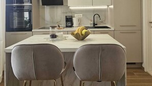 A modern kitchen with a central island, bar stools, a flat-screen TV, and pendant lighting.