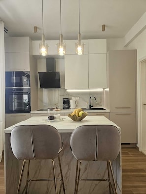 Una cocina moderna con una isla central, taburetes de bar, un televisor de pantalla plana e iluminación colgante.