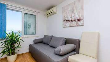 A modern living room with a grey sofa, a white armchair, a large potted plant, and a sailboat painting on the wall.