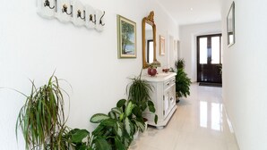 A hallway with a white wall, a white cabinet with plants, a mirror, and framed pictures. - Rooms Mozara (Dubrovnik)