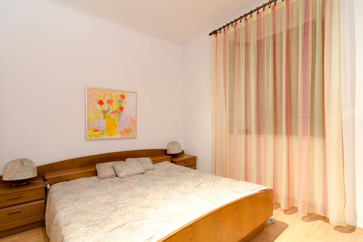 A bedroom with a wooden bed, a nightstand, a lamp, and a painting on the wall.