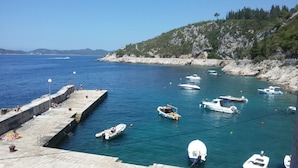 A coastal marina with boats docked, a stone pier with people, and a hilly backdrop. - Rooms Mozara (Dubrovnik)