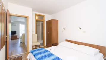A hotel room with a bed, a wooden wardrobe, a seating area with a chair, and a television in the corner.