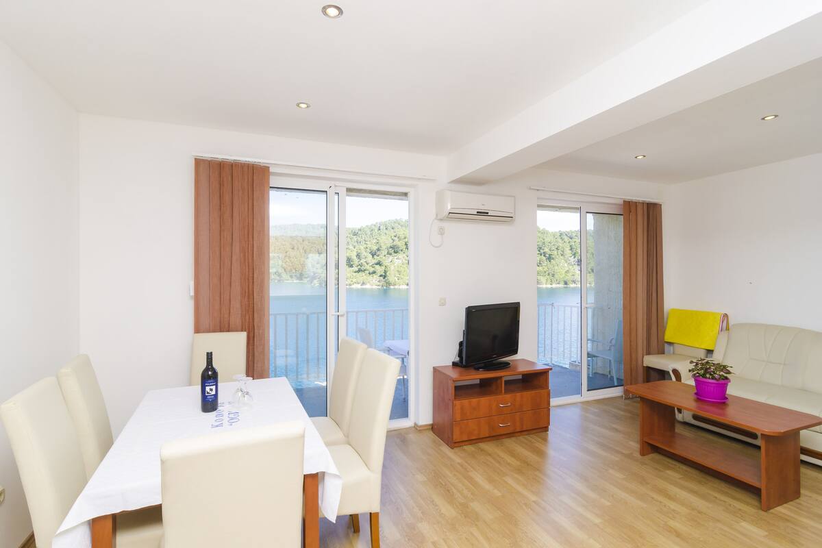 A modern living room with a dining area, a television, and a balcony with a view of the outdoors.