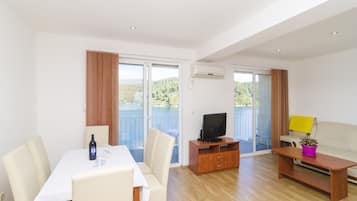 A modern living room with a dining area, a television, and a balcony with a view of the outdoors.