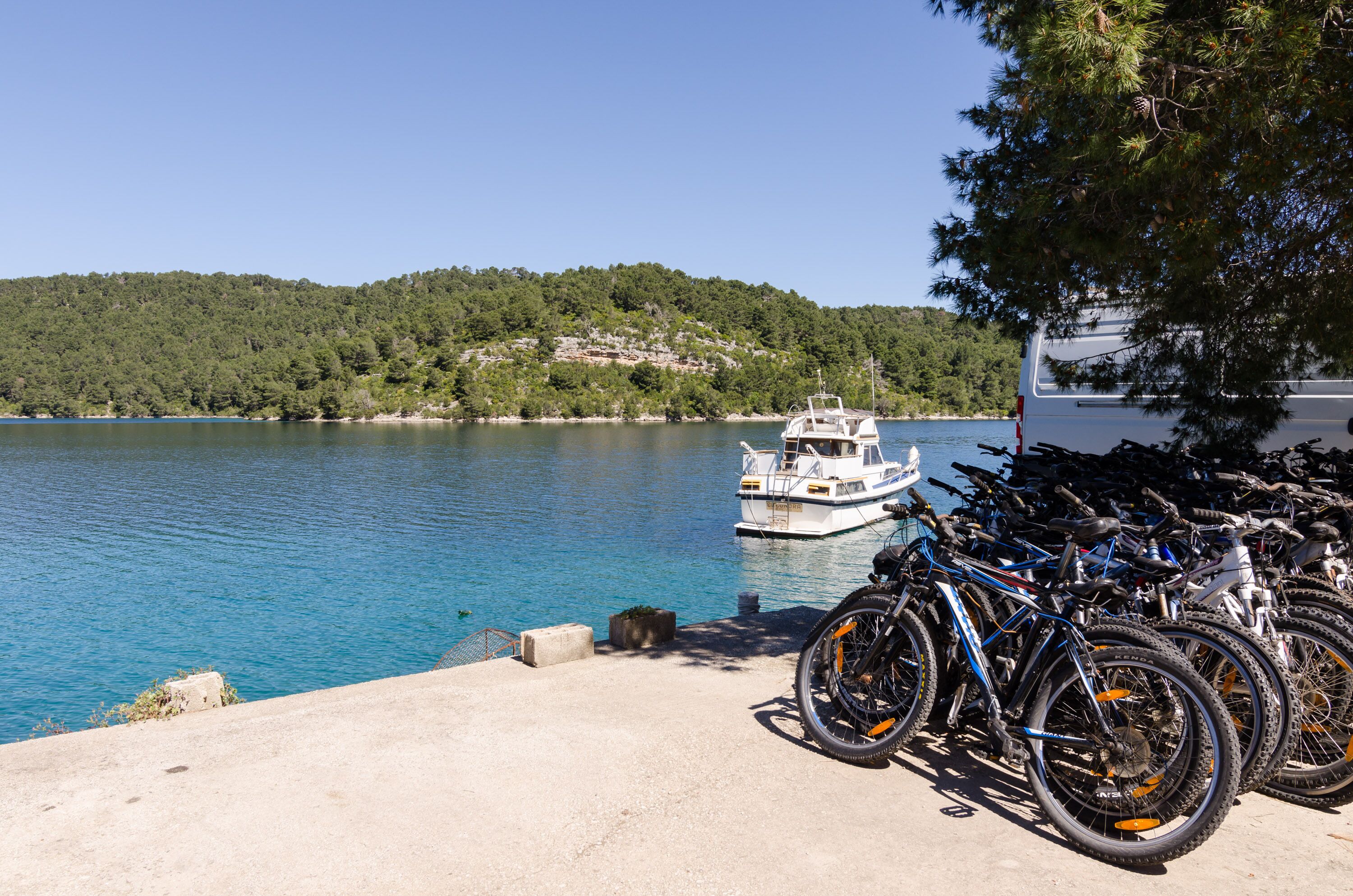 A dock with bicycles and a boat on a calm lake, surrounded by trees and hills.