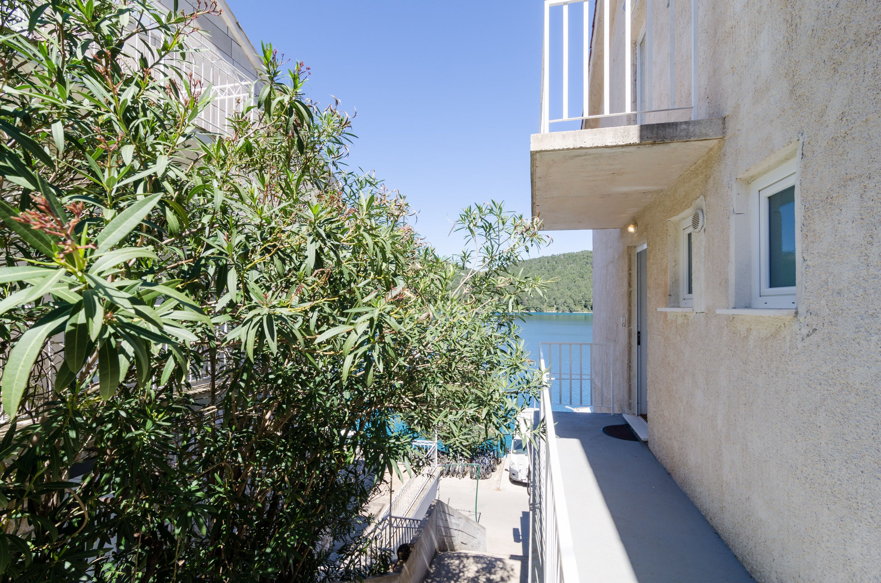 A narrow balcony with a white railing, overlooking a street with a building in the background.