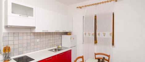 A compact kitchen with white cabinets, a red countertop, a built-in oven, and a small refrigerator.