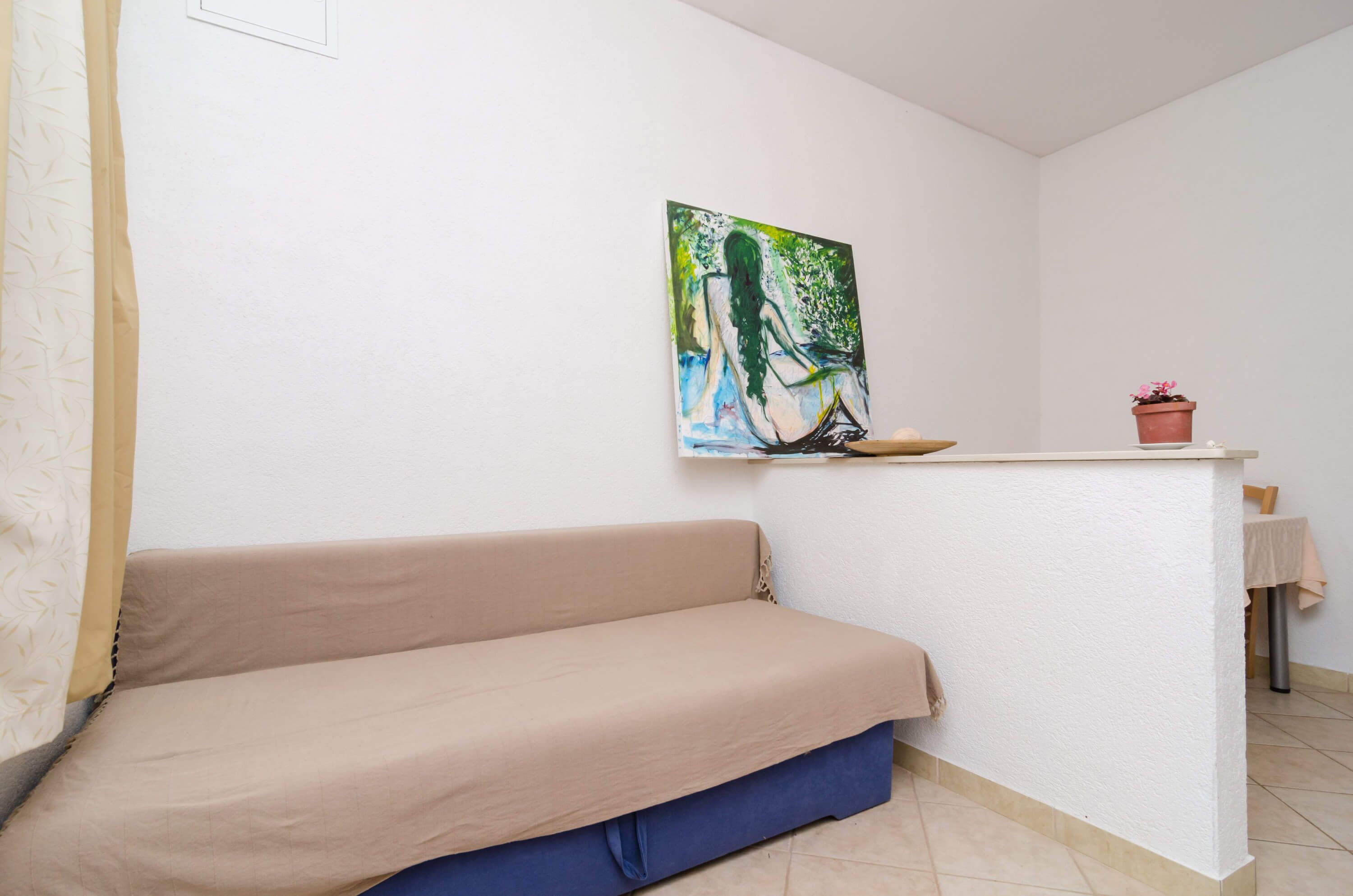 Una habitación con un sofá color beige, una mesita con una planta en maceta y un cuadro en la pared.