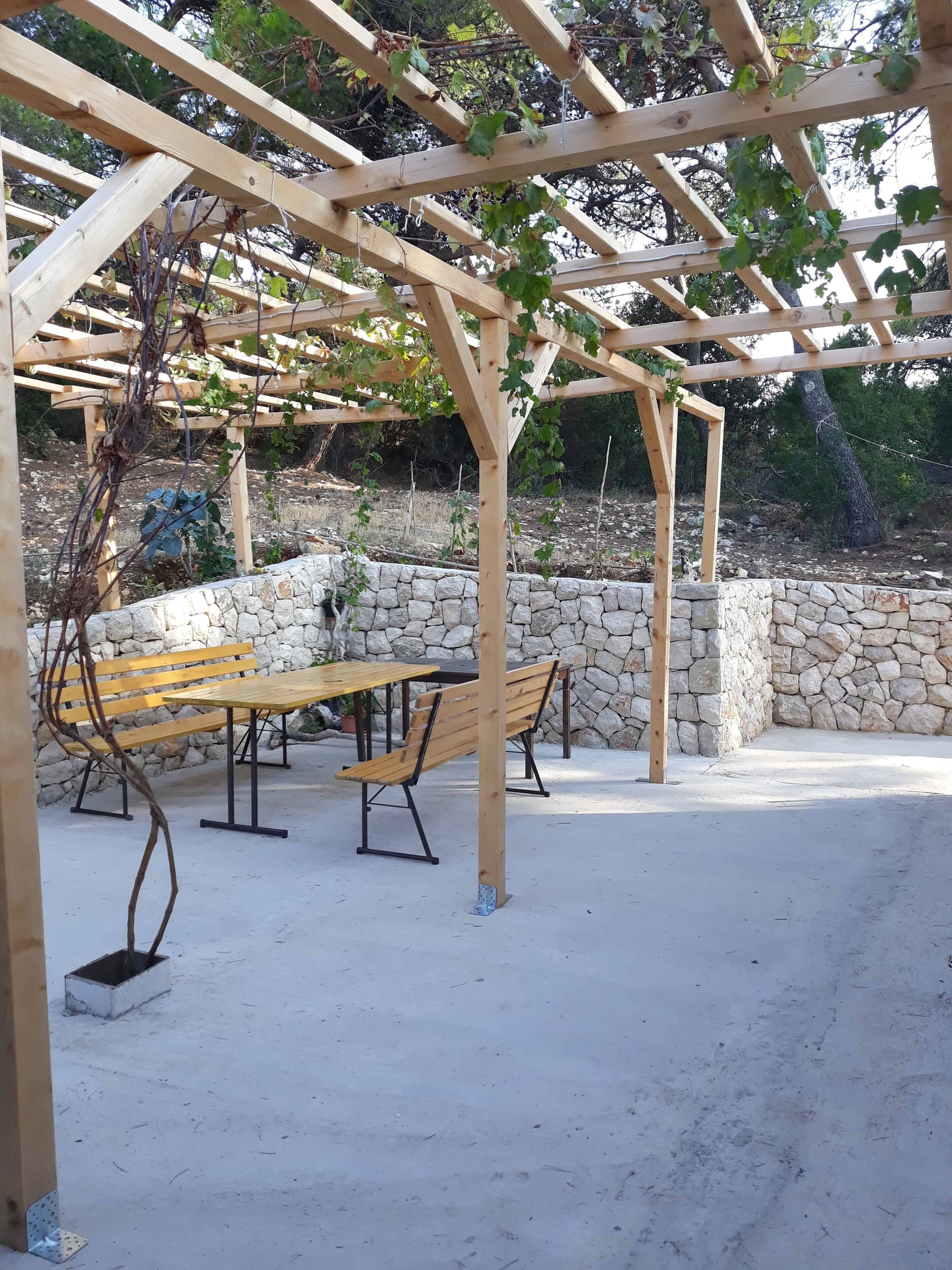 Una pérgola de madera con un muro de piedra y una zona de banco.