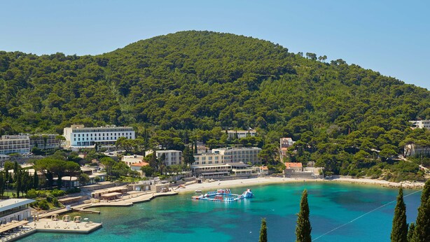 Un pueblo costero con una playa, un muelle para barcos y edificios con balcones con vistas al mar.
