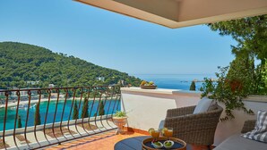 Un balcón con vista a una playa y al mar, muebles de mimbre y una mesa con frutas y bebidas.