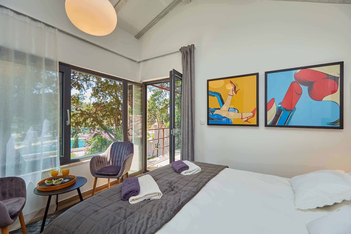 A hotel room with a bed, two chairs, a small table with a tray of orange juice, and two paintings on the wall.