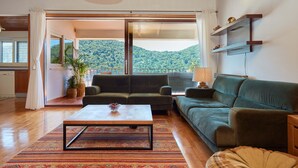 Un espacio habitable amplio con sofá, una mesa de centro y vistas a un paisaje montañoso a través de amplios ventanales.
