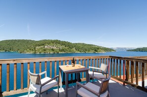 A deck with two chairs and a table, overlooking a lake with a forested island in the distance.